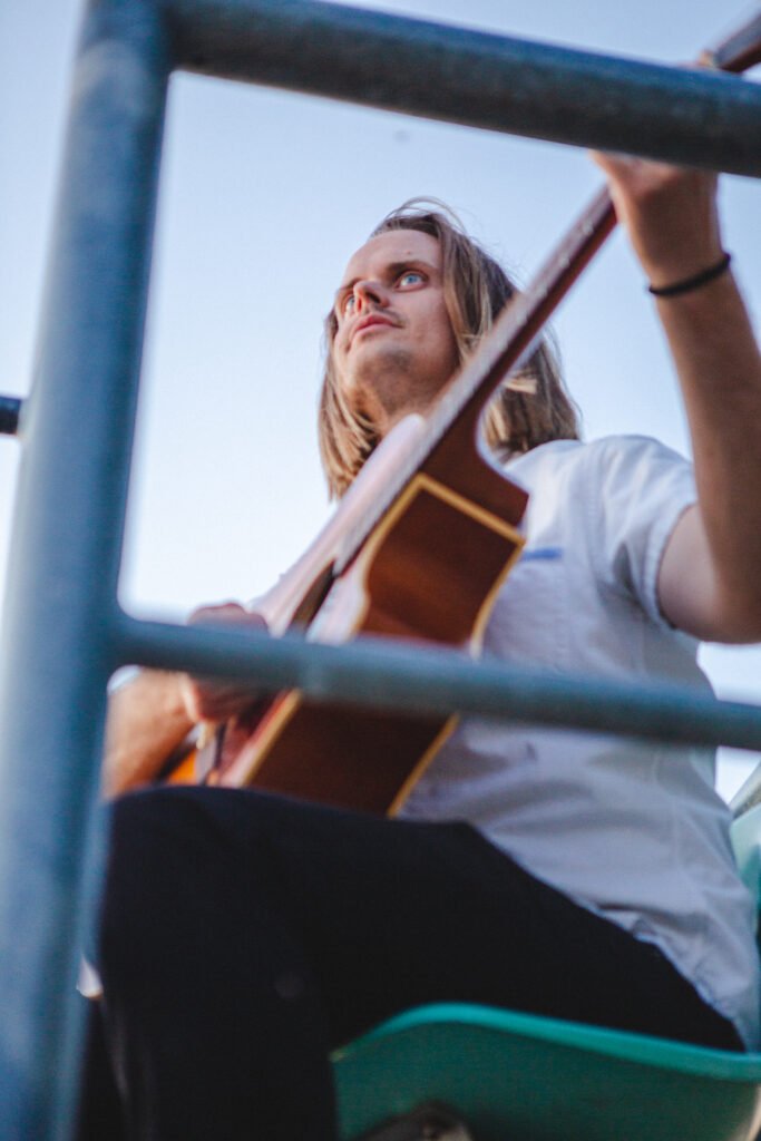 Jack Uppling playing acoustic guitar during an outdoor performance, showcasing his experience as a guitar teacher and songwriter in Portland.