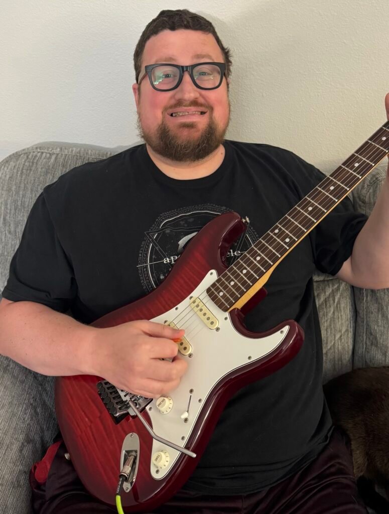 Drew Miller smiling while playing electric guitar, a guitar and piano teacher serving students in the Portland area.
