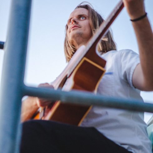 Jack Uppling playing acoustic guitar during an outdoor performance, showcasing his experience as a guitar teacher and songwriter in Portland.