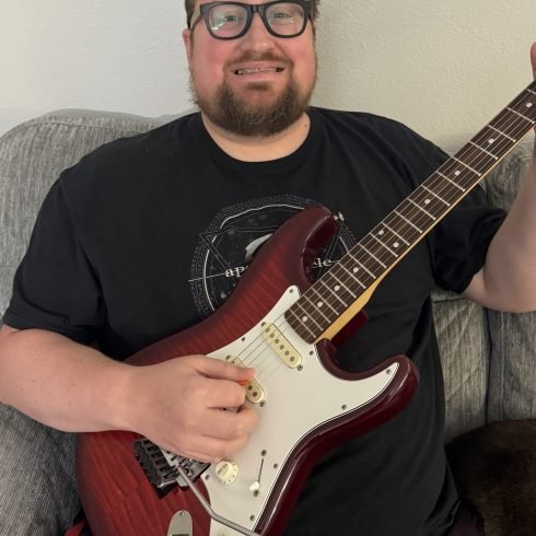 Drew Miller smiling while playing electric guitar, a guitar and piano teacher serving students in the Portland area.